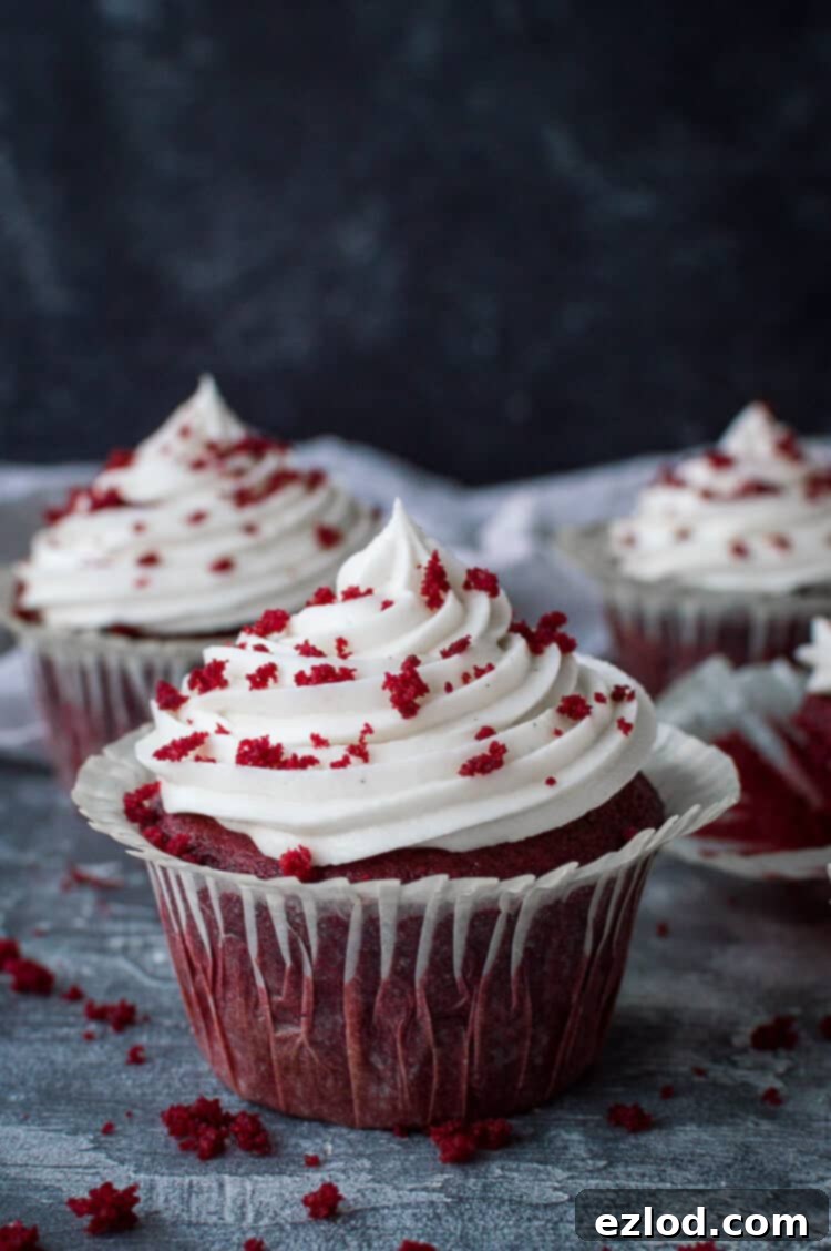 Three vegan red velvet cupcakes with cream cheese frosting on a grey background.