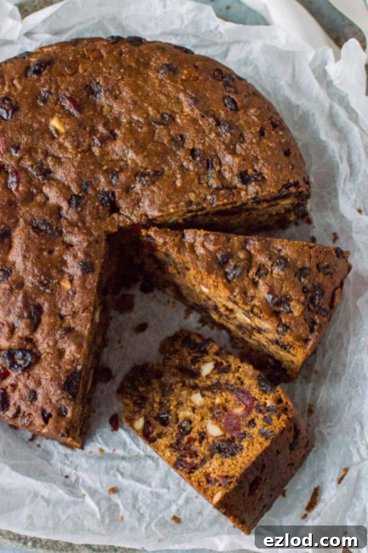 Top-down view of a beautifully sliced vegan Christmas cake, elegantly adorned with fresh cranberries and fragrant rosemary sprigs, against a festive background, ready to be served.