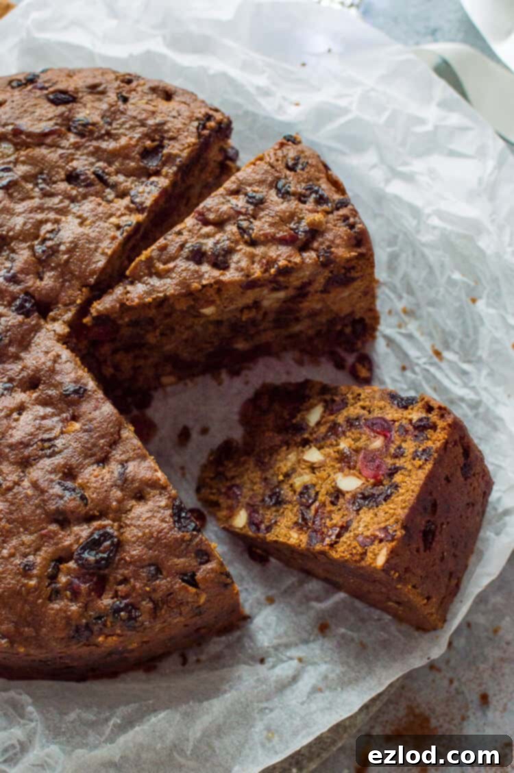 A delicious slice of vegan Christmas fruitcake revealing a dense texture packed with succulent dried fruits and crunchy almonds, presented on a clean white background. This moist vegan fruitcake is a holiday favorite.
