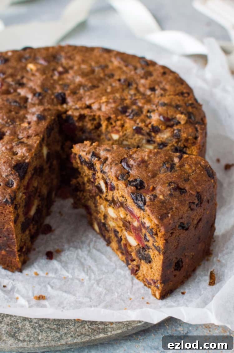 Close-up of a perfectly sliced piece of vegan Christmas fruitcake, showcasing its moist texture and rich dried fruit content, served on white baking parchment. A truly indulgent holiday dessert.