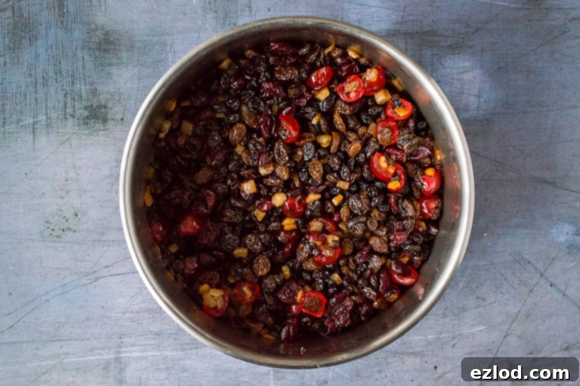 Step 1: A large bowl filled with an assortment of dried fruits, including raisins, sultanas, and cranberries, generously soaking in rum or brandy under a lid, essential for a rich vegan Christmas cake.