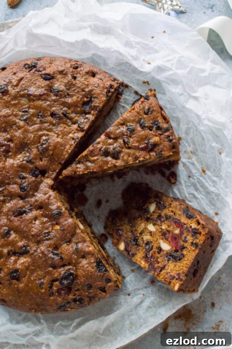 A beautifully presented slice of vegan Christmas fruitcake on white baking parchment, showcasing its rich, dense, and fruit-filled texture, ready to be enjoyed as a festive dessert.