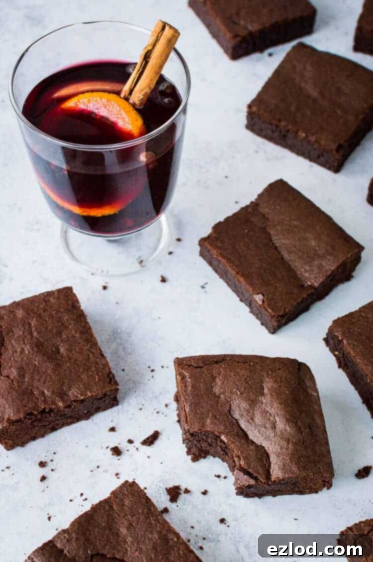 Vegan mulled wine brownies on a grey background with a glass of mulled wine with orange slices and a stick of cinnamon.