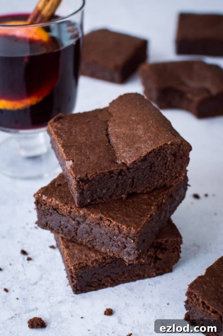 A stack of three fudgy vegan mulled wine brownies with a glass of mulled wine in the background.