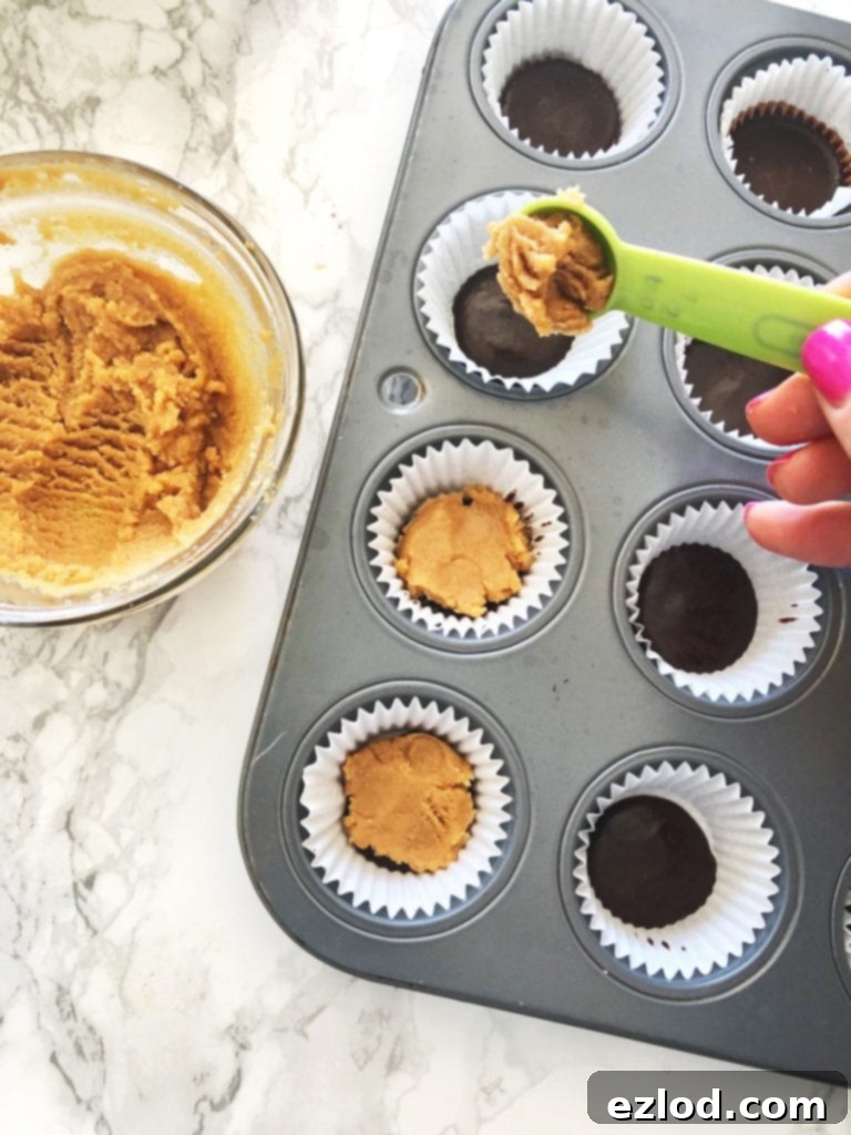 Making healthy mini copy cat peanut butter cups by layering a peanut butter mixture over some chocolate in a mini muffin tin