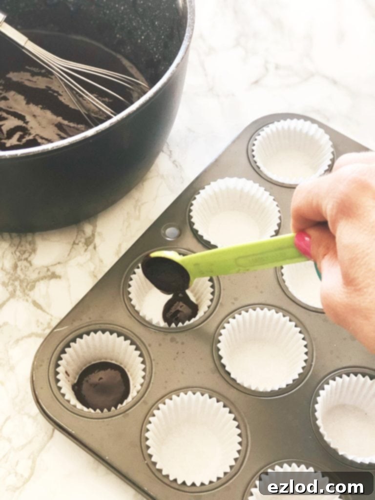 Filling a mini cupcake tin lined with paper liners with homemade chocolate for Reese's peanut butter cups 