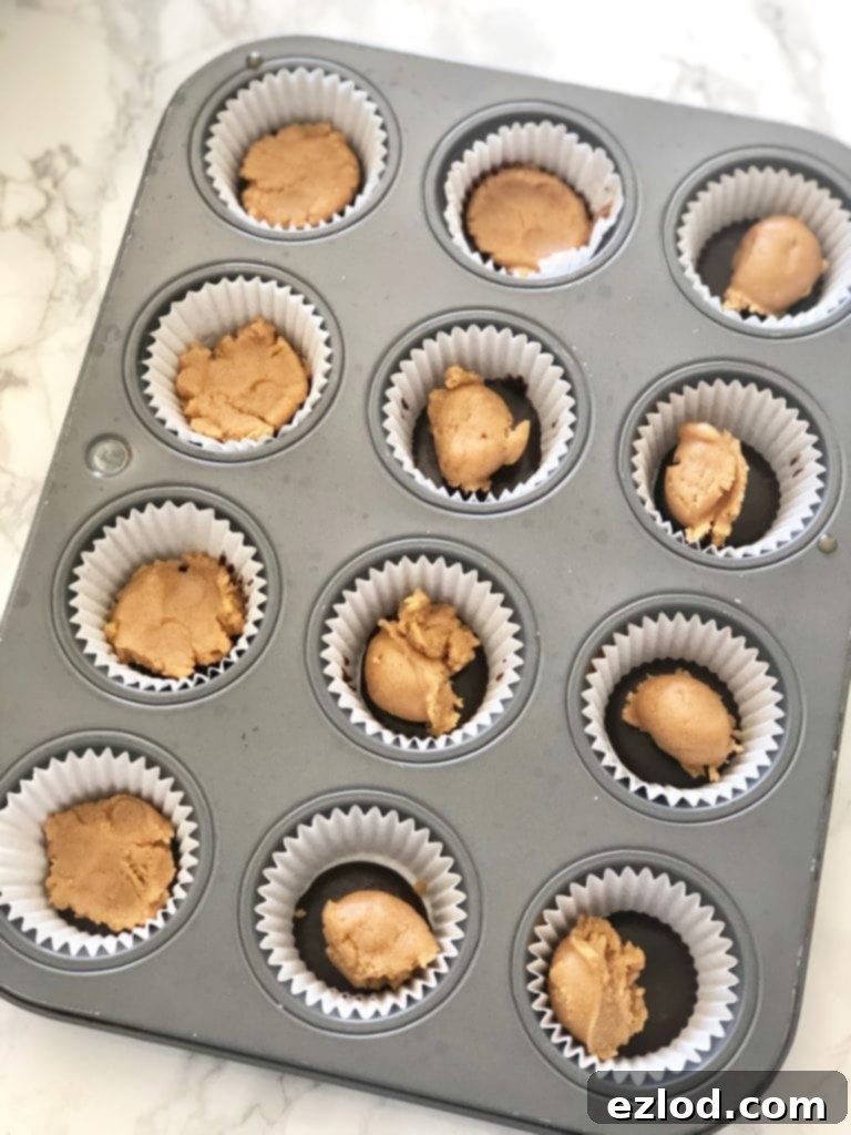 A mini cupcake tin lined with paper liners and a layer of chocolate and peanut butter for mini peanut butter cups 