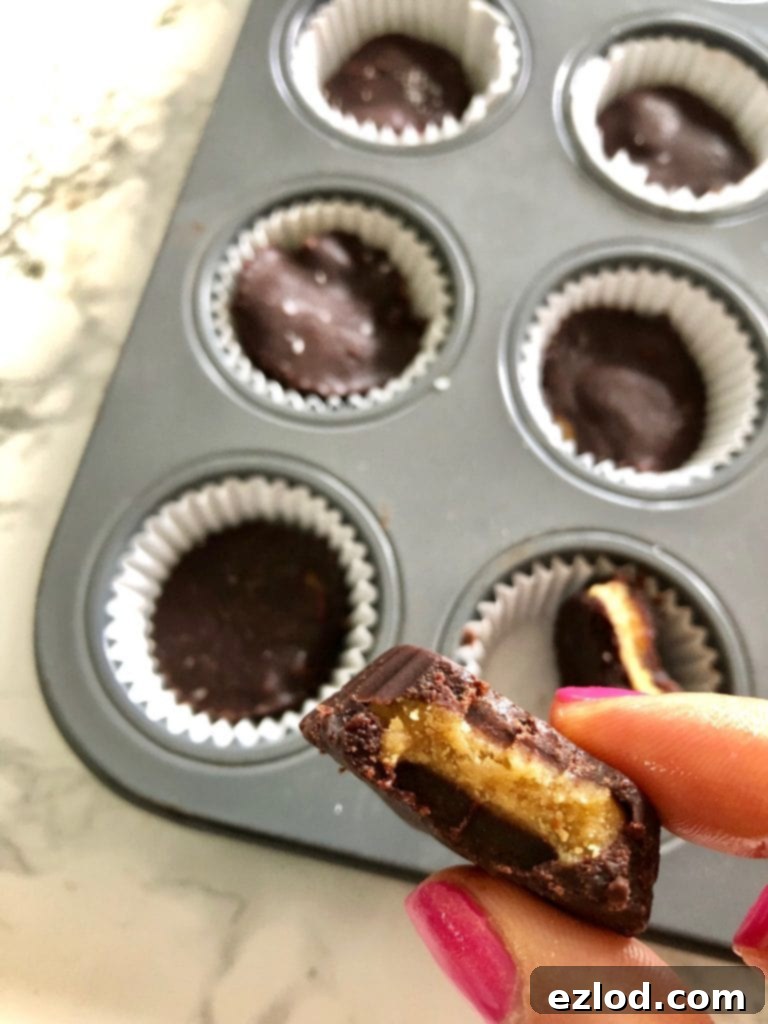 A close up of a mini homemade peanut butter cup, a whole mini muffin tray is in the background filled with finished peanut butter cups