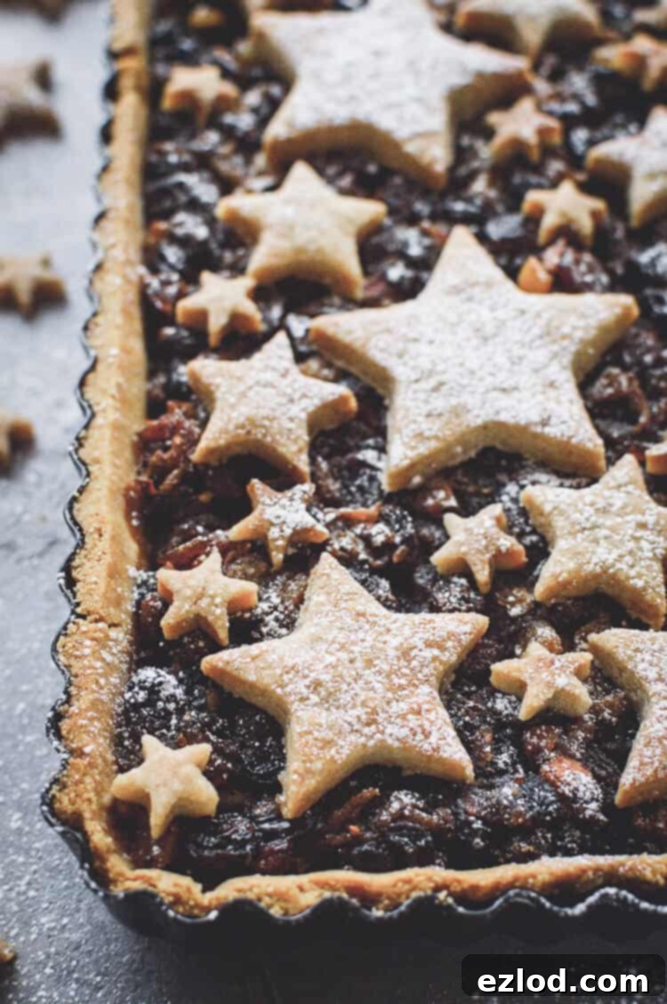 An inviting angled close-up shot of a slice of the vegan mince pie tart, showcasing its intricate topping of cinnamon shortbread stars. The golden crust and rich mincemeat filling are visible, highlighting the delicious texture and festive appeal of this unique Christmas dessert.