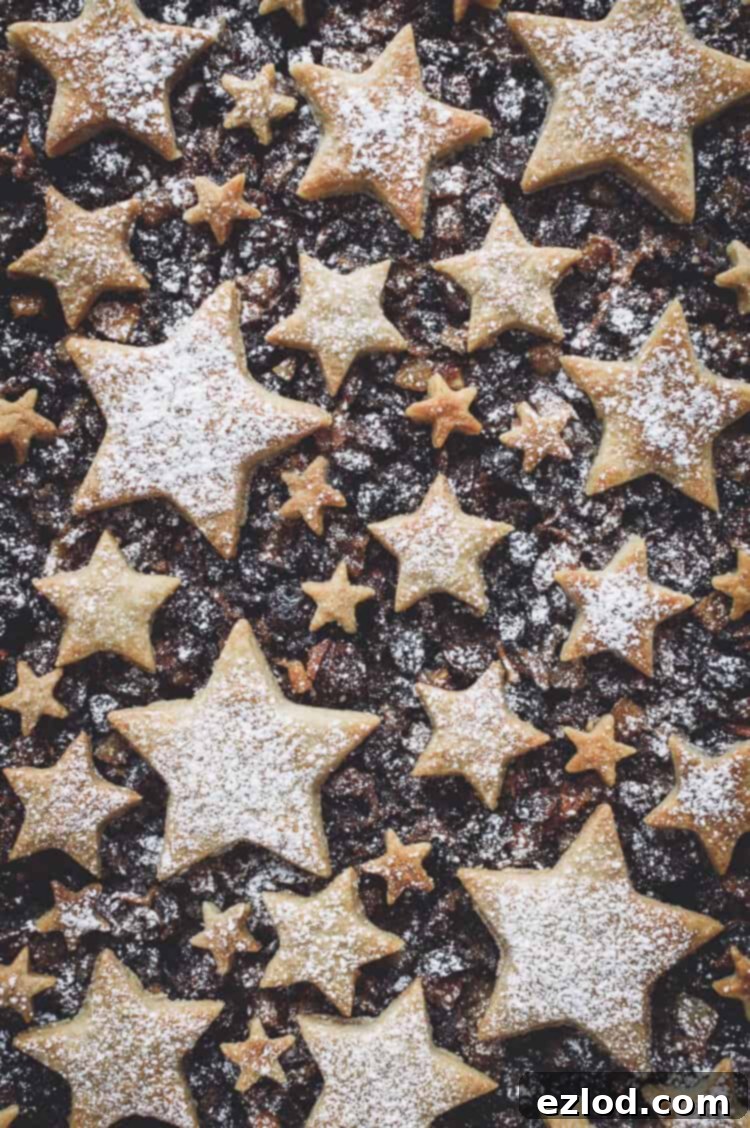 A detailed close-up of the vegan mince pie tart, emphasizing the charming cinnamon shortbread stars arranged artfully on top of the rich mincemeat filling. The edges of the tart are golden and inviting, making it a mouth-watering festive dessert.
