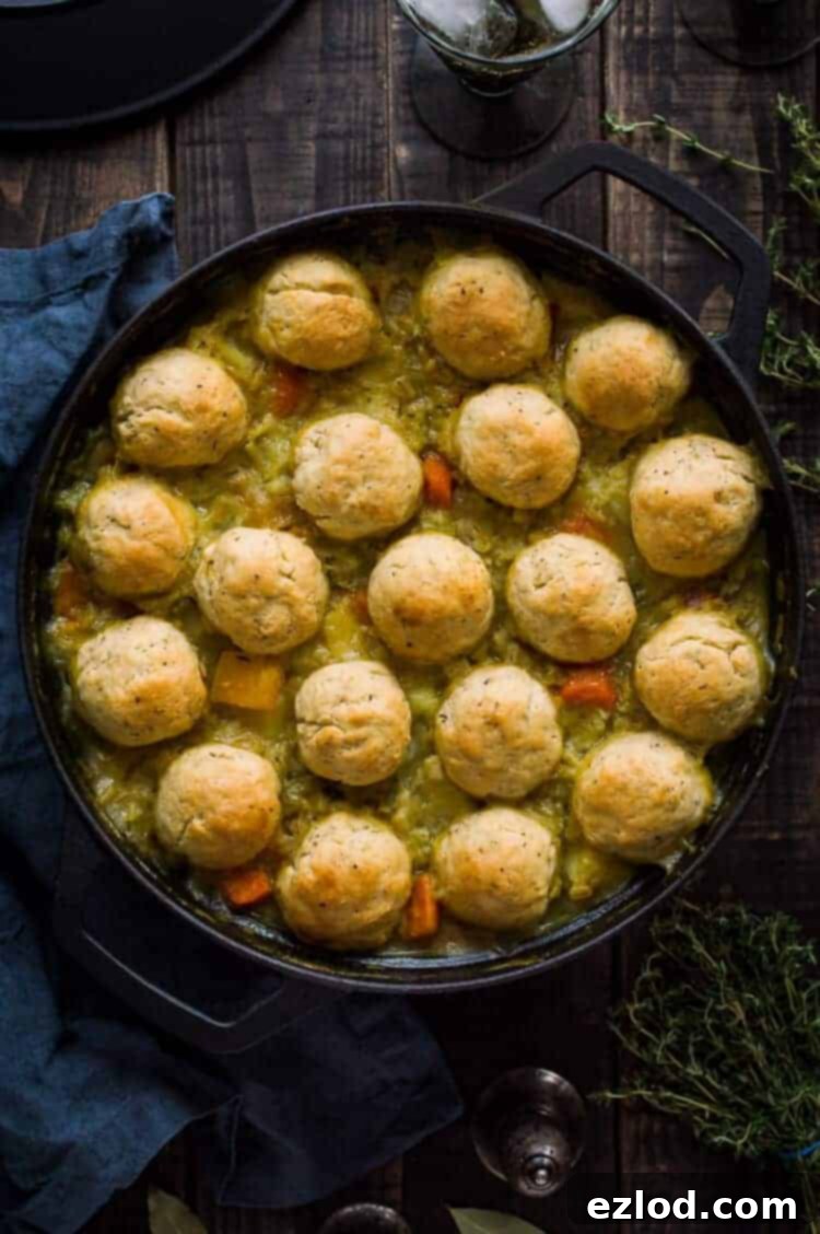 A vibrant, steaming bowl of vegan winter vegetable and pearl barley stew, generously topped with golden brown, fluffy herby dumplings. The rustic background suggests a cozy, cold-weather meal setting.
