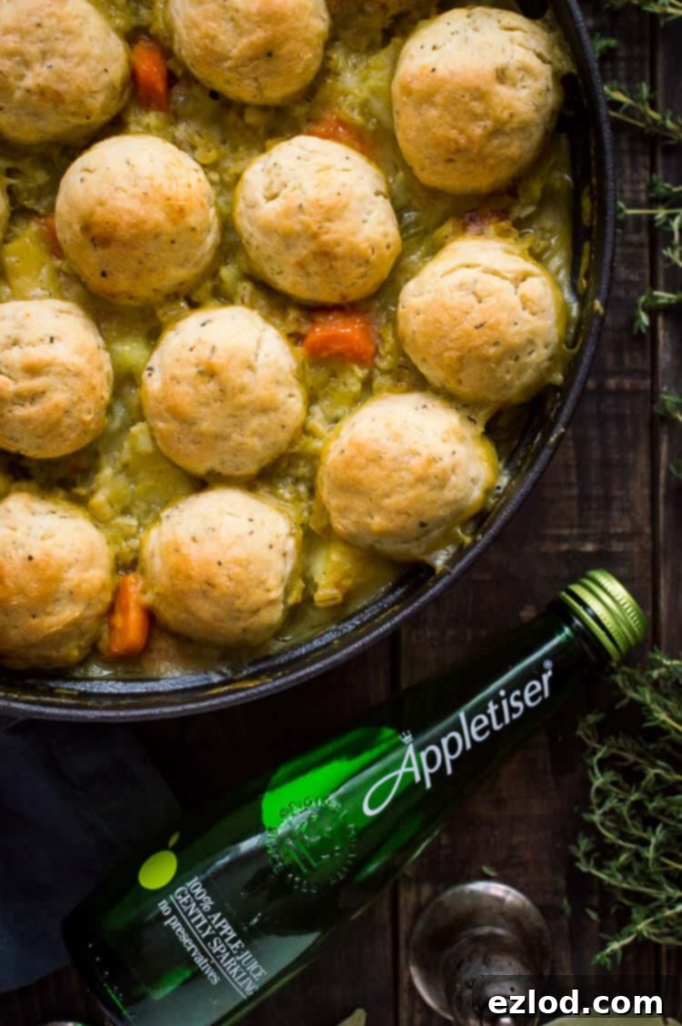 A close-up view of the simmering vegetable and pearl barley stew, showcasing its thick, rich texture and the hearty ingredients. Fresh herby dumplings are nestled on top, ready to absorb the flavors, with an Appletiser bottle in soft focus.