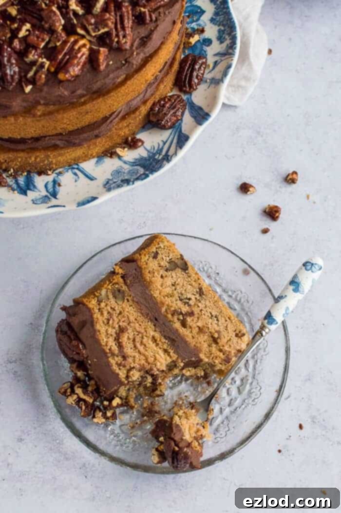 A beautifully decorated vegan maple pecan cake with a generous layer of chocolate cashew cream frosting, garnished with maple pecans. The cake sits on a rustic white plate, embodying a delightful and healthier dessert option.
