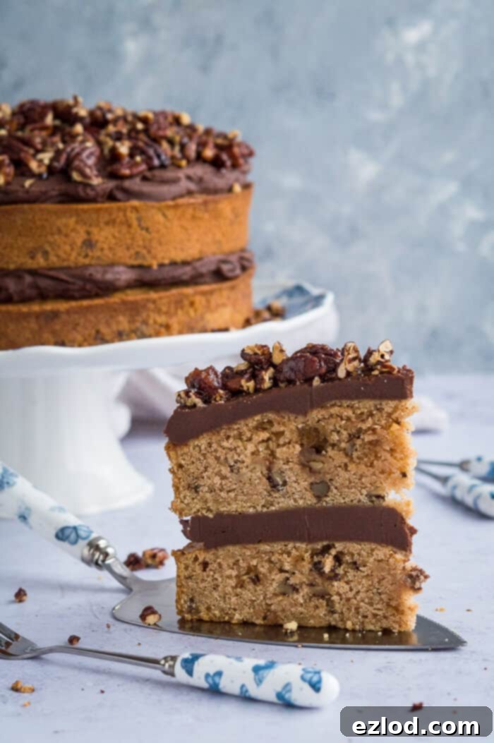A perfectly sliced piece of vegan maple pecan cake with layers of chocolate cashew cream frosting, presented on a cake server, with the remaining cake visible in the background.