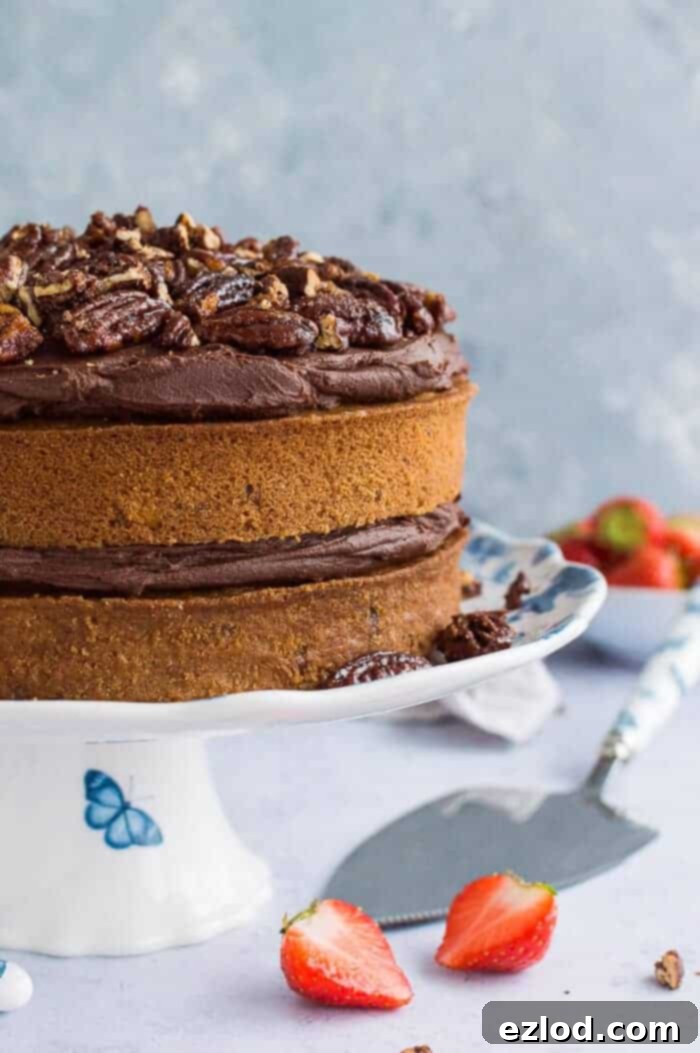 Side view of a luscious two-layer vegan maple pecan cake, generously frosted with smooth chocolate cashew cream and topped with crunchy maple-glazed pecans, presented on an elegant blue and white cake stand.