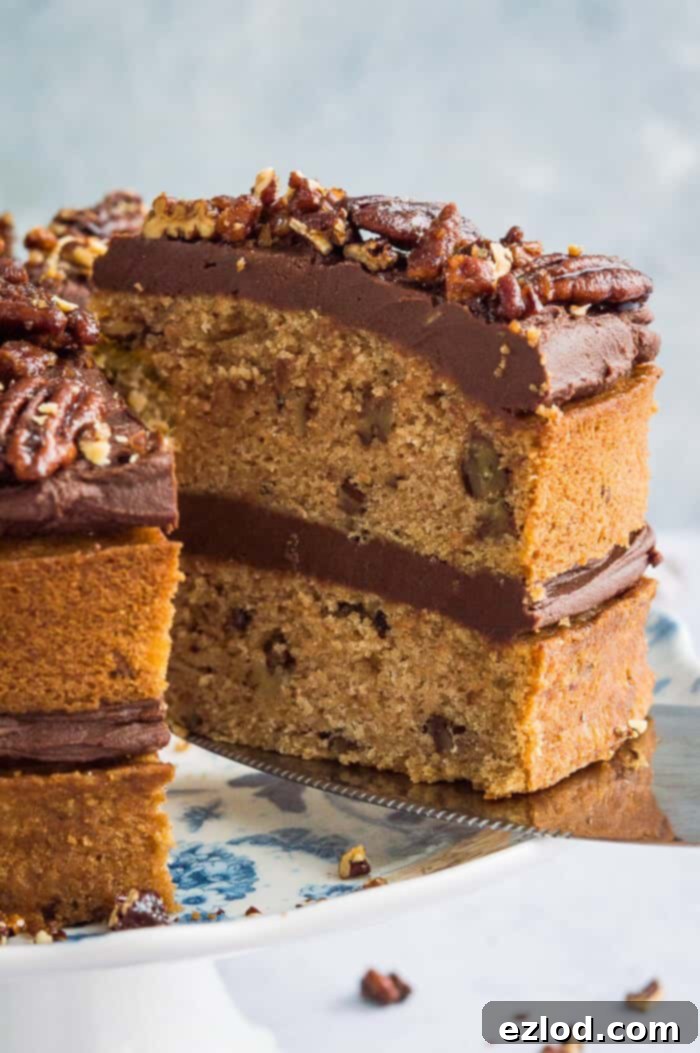 Close-up shot of a single slice of vegan, naturally sweetened maple pecan cake, showcasing its moist texture, layered with creamy chocolate cashew frosting and topped with glistening maple pecans.