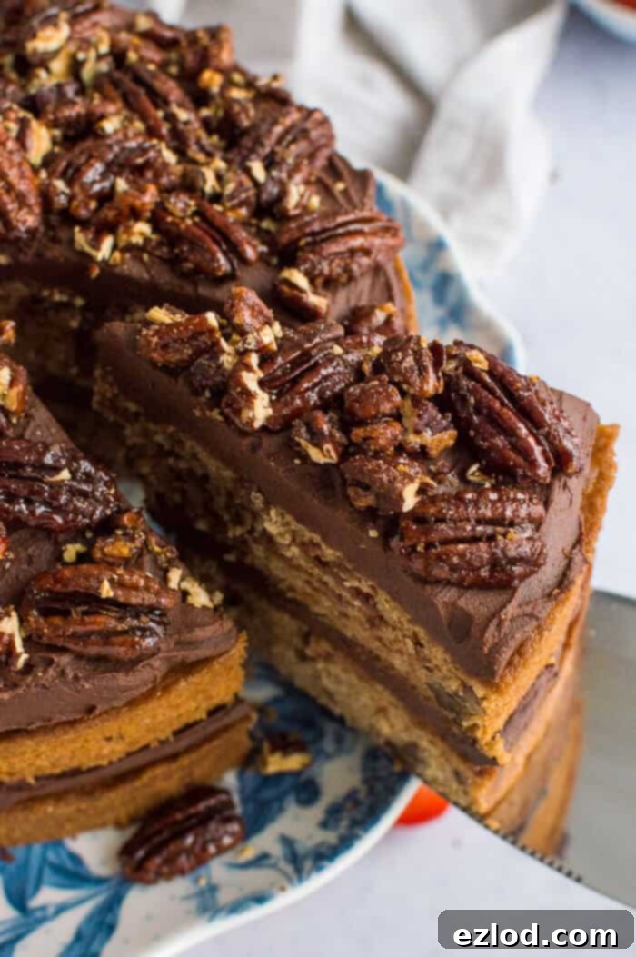 Close-up of crunchy, golden maple pecans artfully scattered on top of a vegan maple pecan cake, contrasting with the smooth chocolate cashew cream frosting beneath.