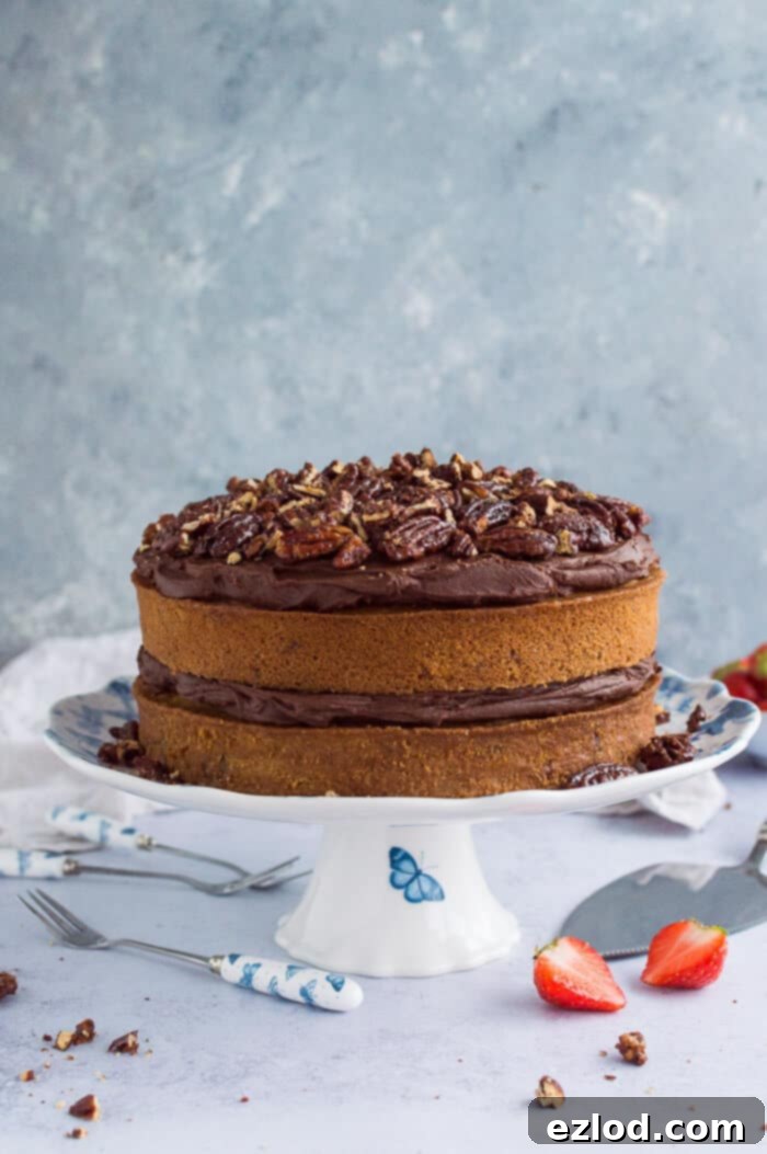 A complete vegan maple pecan cake with chocolate cashew cream frosting, presented on a blue and white cake stand against a grey background, ready to be served.
