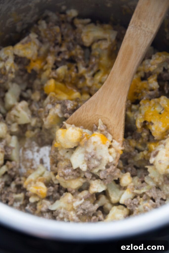 Close-up of a serving of creamy, cheesy Instant Pot Cauliflower Cheeseburger Mac in a bowl, showing the texture of the cauliflower and ground beef.