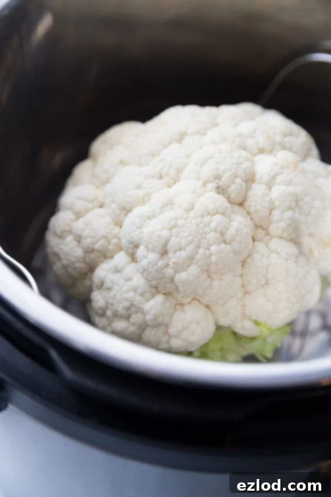 A whole head of cauliflower placed on a trivet inside an Instant Pot, ready for steaming.