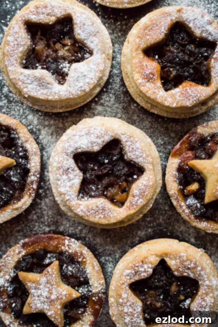 a close up of vegan mince pies with coconut oil pastry dusted with icing sugar on a black background.