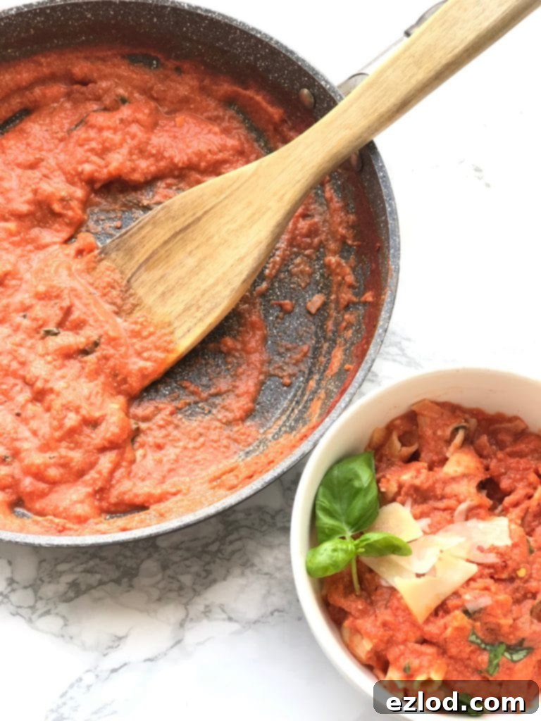 A pan of fresh vodka sauce with a wooden spoon, next to a bowl of penne, vodka sauce and chicken, topped with Parmesan cheese and basil.