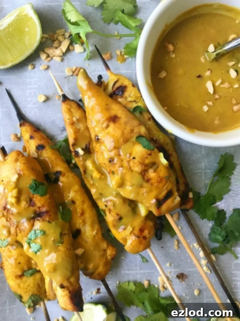Chicken Satay Skewers on a Baking Pan with creamy peanut sauce, crushed peanuts, and lime wedges for grilling