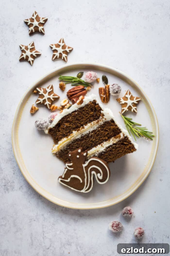A slice of vegan ginger layer cake with vegan gingerbread woodland animal cookies, sugared cranberries, rosemary, nuts and seeds. The cake features three moist layers, vegan cream cheese frosting, and zesty lemon curd.