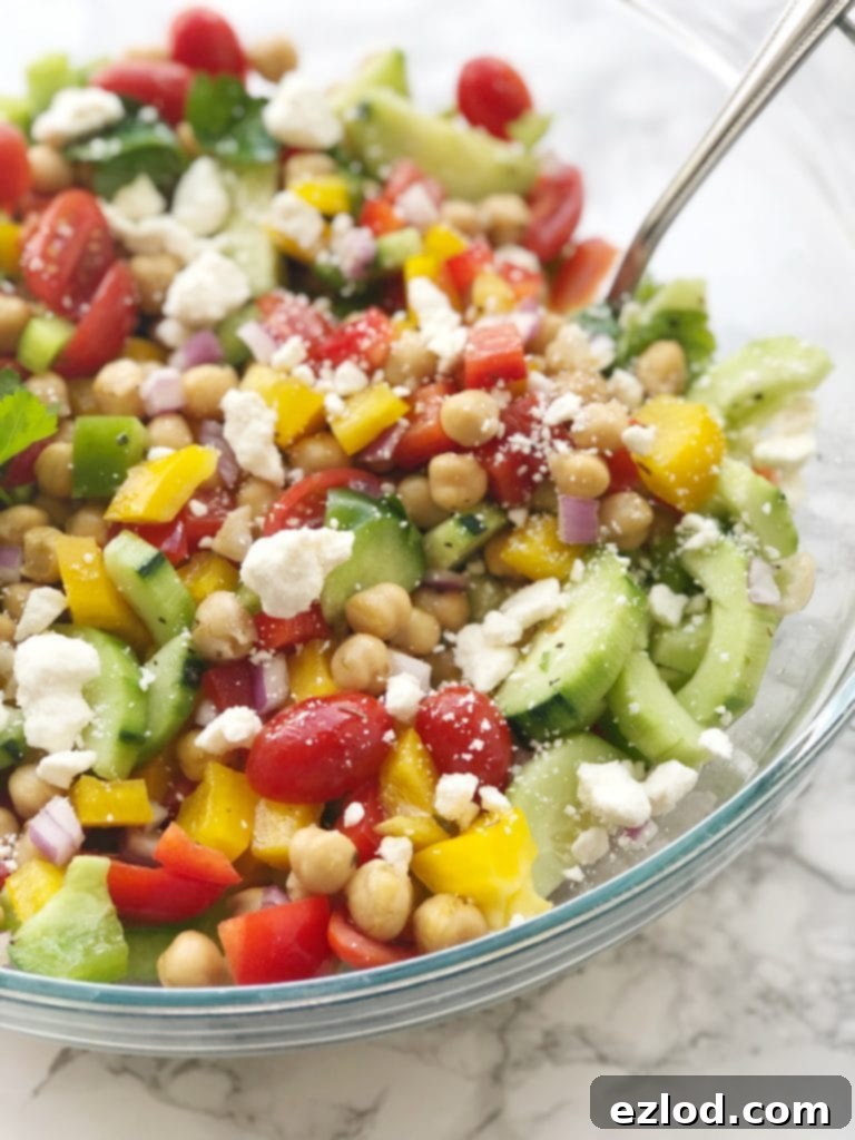 A close up shot of a healthy and vibrant Mediterranean Chickpea Salad in a glass bowl, garnished with a sprinkle of feta cheese, ready for a delicious meal.