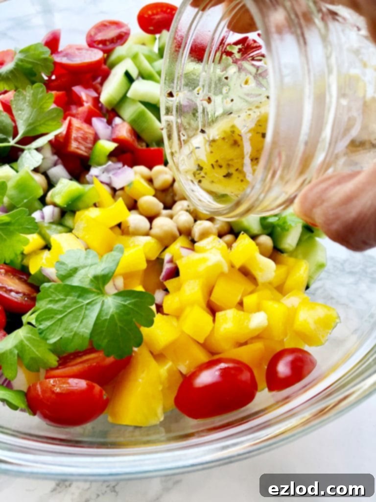 Homemade Greek dressing being poured over a bowl of fresh chickpeas and colorful chopped veggies for a healthy 21 Day Fix Greek Salad.