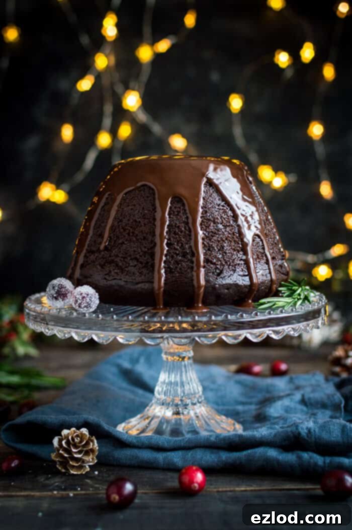 Lush vegan steamed chocolate pudding on a glass cake stand, adorned with delicate fairy lights in the background, creating a festive and inviting atmosphere.