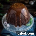Decadent Vegan Steamed Chocolate Pudding 14 Vegan steamed chocolate pudding topped with chocolate sauce on a glass plate on a wooden background.