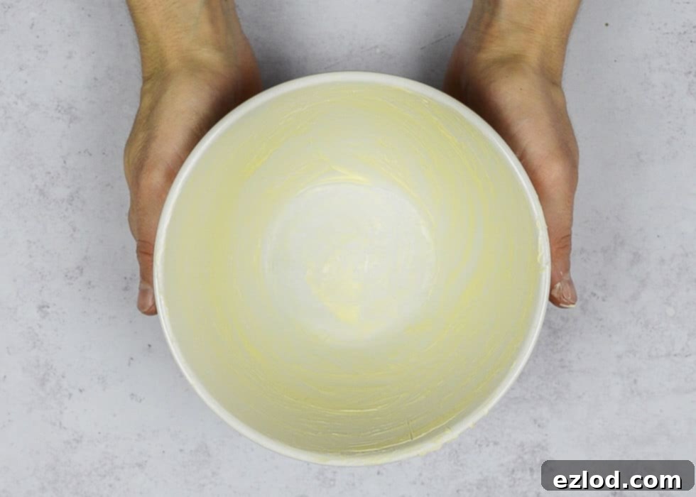 Step 1: Preparing the pudding basin by greasing thoroughly and lining the bottom with a disc of baking parchment, with a kettle boiling in the background.