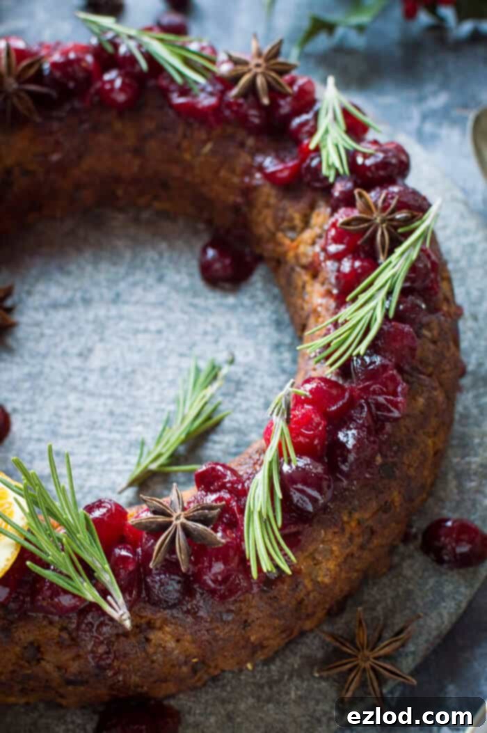 Close up of a festive vegan nut roast wreath, elegantly topped with bright cranberry sauce, fresh rosemary sprigs, and fragrant spices, highlighting its rich texture and appealing presentation.