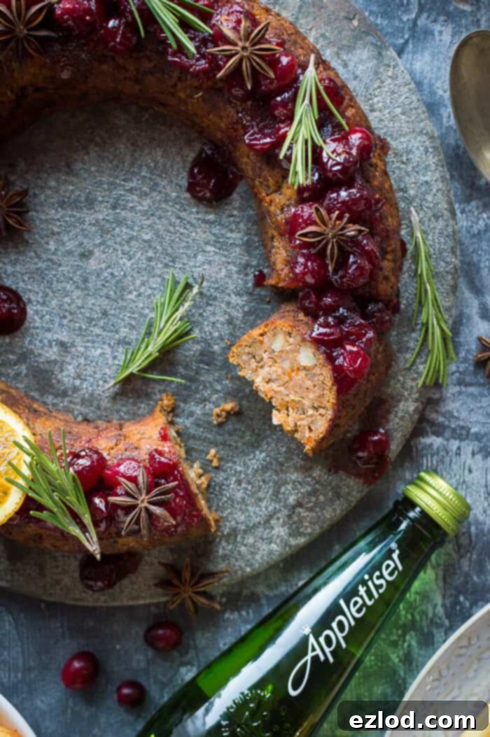 A beautifully sliced vegan nut roast wreath, showcasing layers of butternut squash, mushrooms, and chestnuts, placed next to a sparkling bottle of Appletiser, perfect for a festive feast.