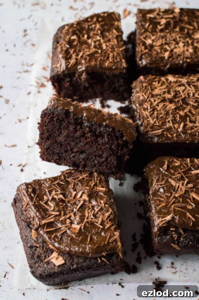 Fudgy Beetroot Chocolate Cake with Avocado Silk Frosting 3 Several squares of vegan beetroot chocolate cake with chocolate avocado frosting and chocolate shavings are artfully arranged on a grey surface, with a close-up focus on the tender crumb of one slice.