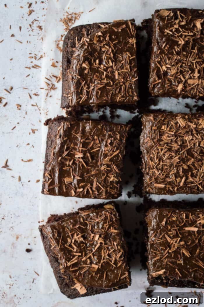 Fudgy Beetroot Chocolate Cake with Avocado Silk Frosting 8 Six squares of vegan beetroot chocolate cake, each topped with creamy chocolate avocado frosting and delicate chocolate shavings, artfully arranged on a neutral grey background.