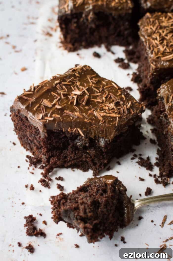 Fudgy Beetroot Chocolate Cake with Avocado Silk Frosting 9 A close-up shot of a single square of vegan beetroot chocolate cake with chocolate avocado frosting and chocolate shavings, with a piece expertly removed by a fork, revealing its moist and fudgy interior.