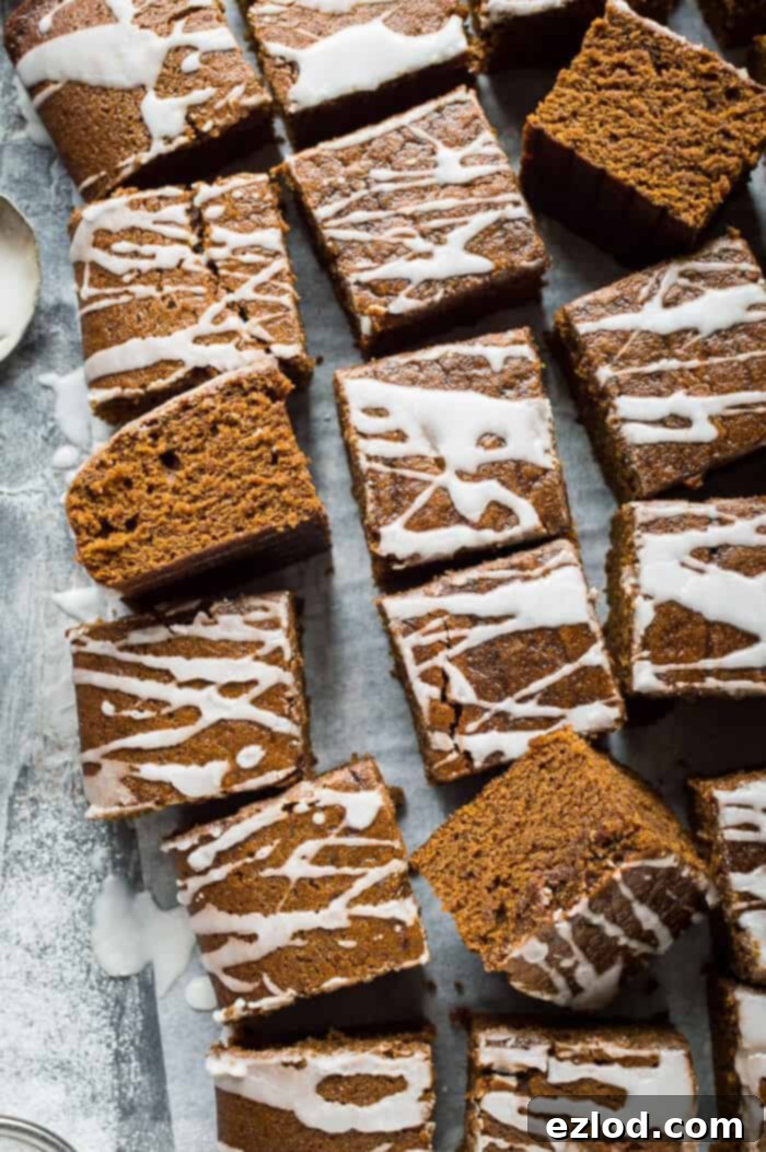 Squares of vegan ginger tray bake cake with lemon glaze on baking parchment on a grey background.