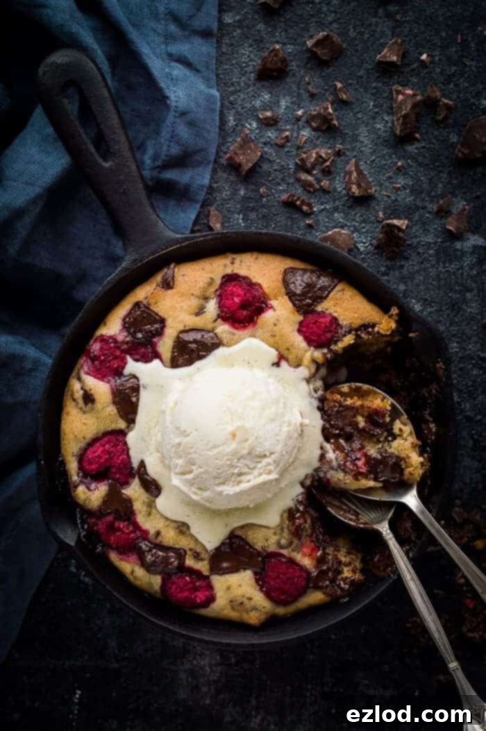 chocolate raspberry cookie in a cast iron skillet topped with ice cream and two spoons.