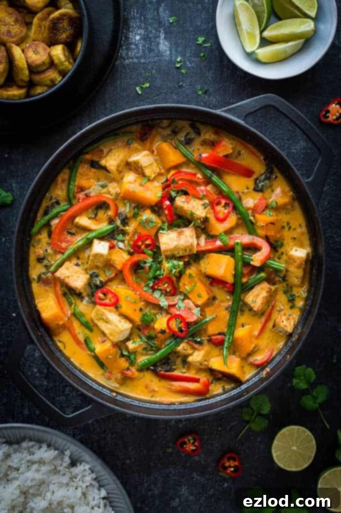A vibrant bowl of vegan tofu moqueca, showcasing fried tofu cubes, butternut squash, red peppers, and green beans in a rich orange-hued coconut sauce, garnished with fresh cilantro.