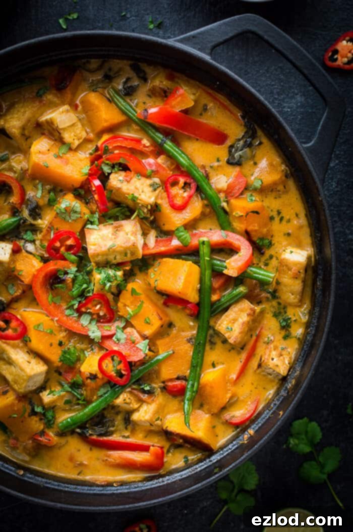 Close-up of a rich, bubbling vegan tofu and vegetable moqueca stew in a black cast iron pan, ready to be served, showcasing its vibrant color and thick texture.