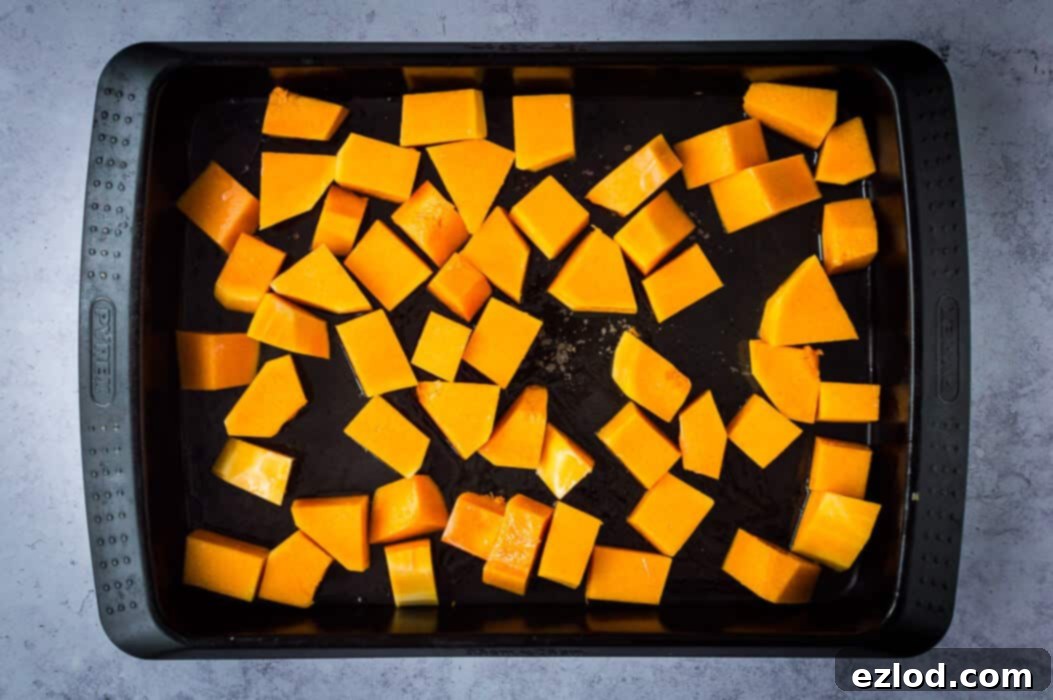 First step in making vegan tofu moqueca: Diced butternut squash is spread on a baking sheet and drizzled with olive oil, ready for roasting.