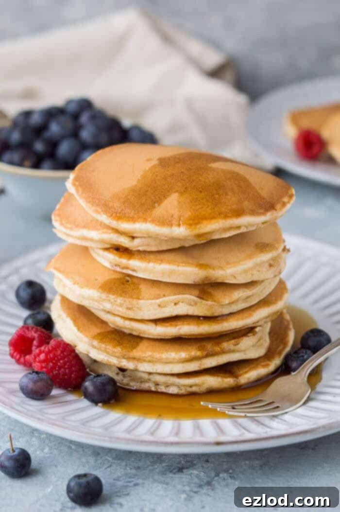 A stack of golden brown, fluffy vegan vanilla pancakes drizzled with maple syrup and topped with fresh berries, showcasing their soft texture. #veganpancakes #vanillapancakes #plantbasedbreakfast #dairyfree #eggfree