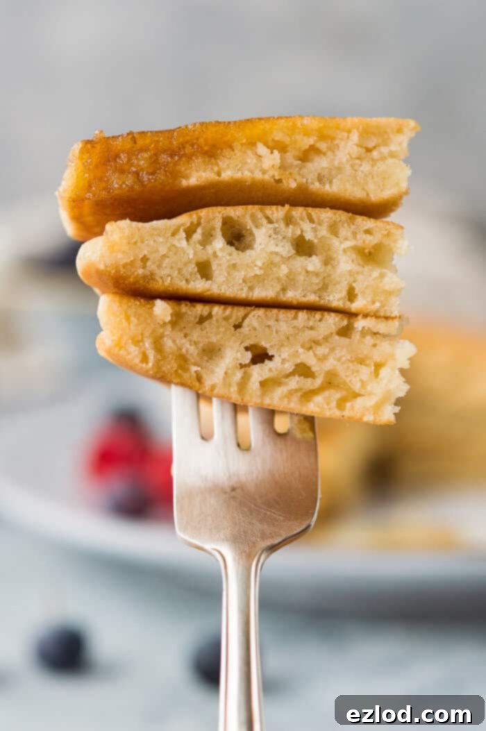 Close-up shot of a fork lifting a slice of fluffy vegan vanilla pancake, showing the tender, airy interior texture.