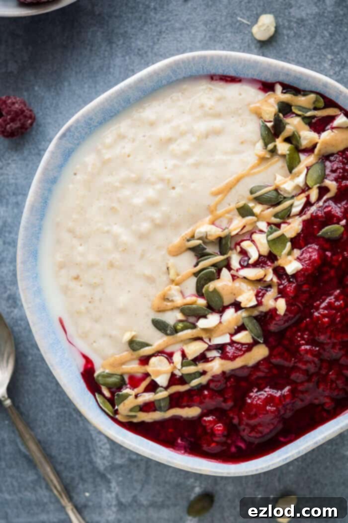 Close up of a bowl of vegan peanut butter porridge topped with raspberry compote, nuts, pumpkin seeds and a drizzle of peanut butter.
