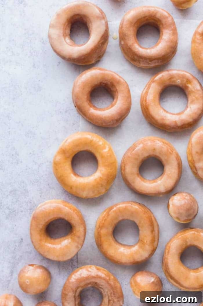 Vegan glazed doughnuts on a sheet of baking parchment on a grey background.
