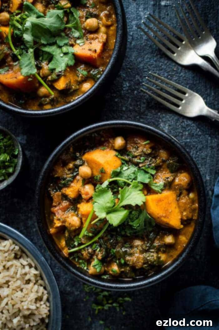 Two black bowls filled with a vibrant orange vegan chickpea, sweet potato, and spinach curry, garnished with fresh coriander, placed on a dark background.
