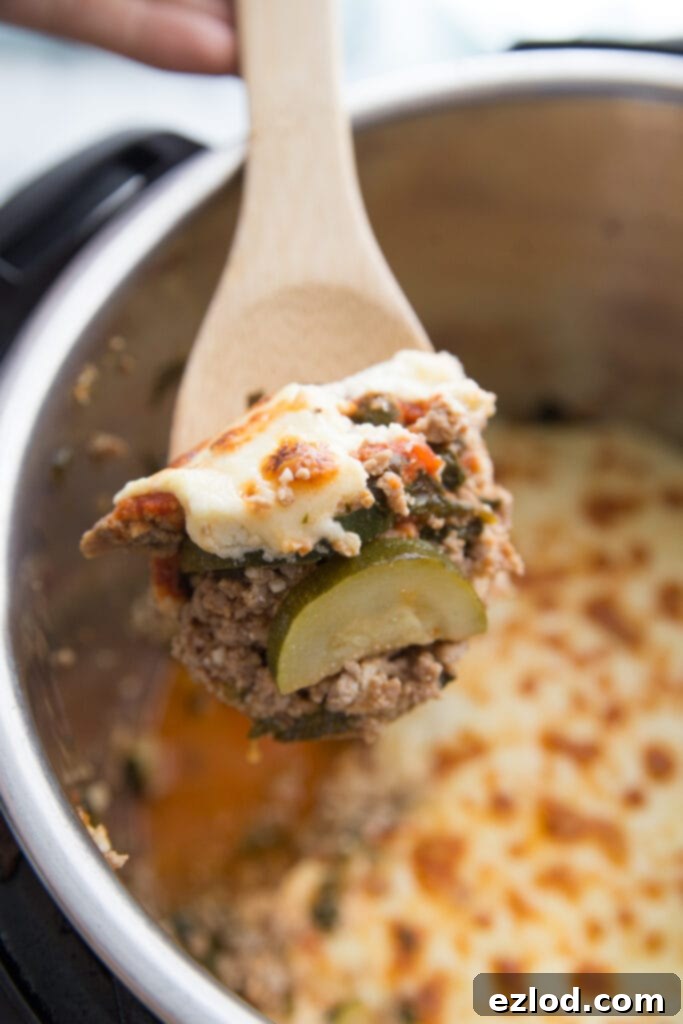 In the foreground, a wooden spoon with a bite of Instant Pot Zucchini Lasagna, showing the layers of zucchini and cheese. In the background (unfocused), an Instant Pot full of lasagna ready to be served. This delicious Instant Pot Zucchini Lasagna is a healthy, low-carb option, perfect for Instant Pot and CrispLid users.