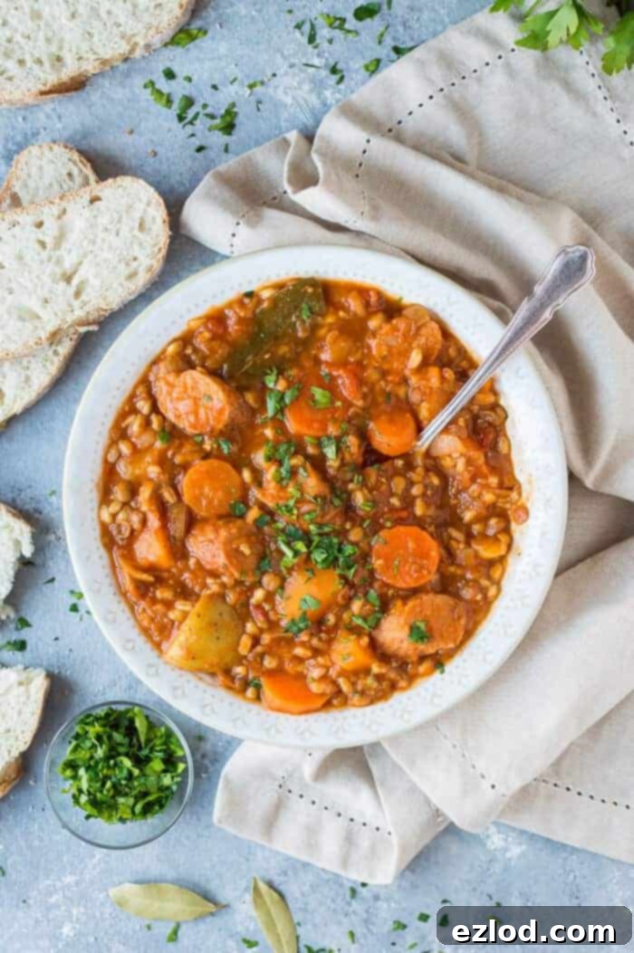 A white bowl full of vegan stew on a grey background with a cream cloth, a bowl of parsley and sliced bread.